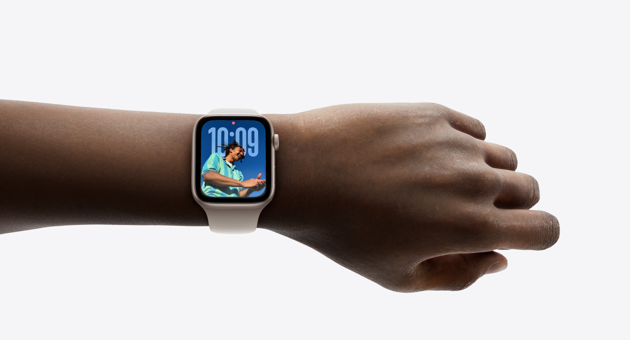 Close-up van Apple Watch in Roségoud met rubberen bandje om iemands pols, waarop het nieuwe Liquid Glass-design zichtbaar is