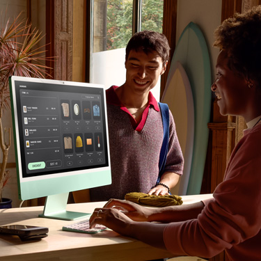 Dans une boutique de surf, une personne derrière le comptoir traite pour quelqu’un une transaction sur iMac.