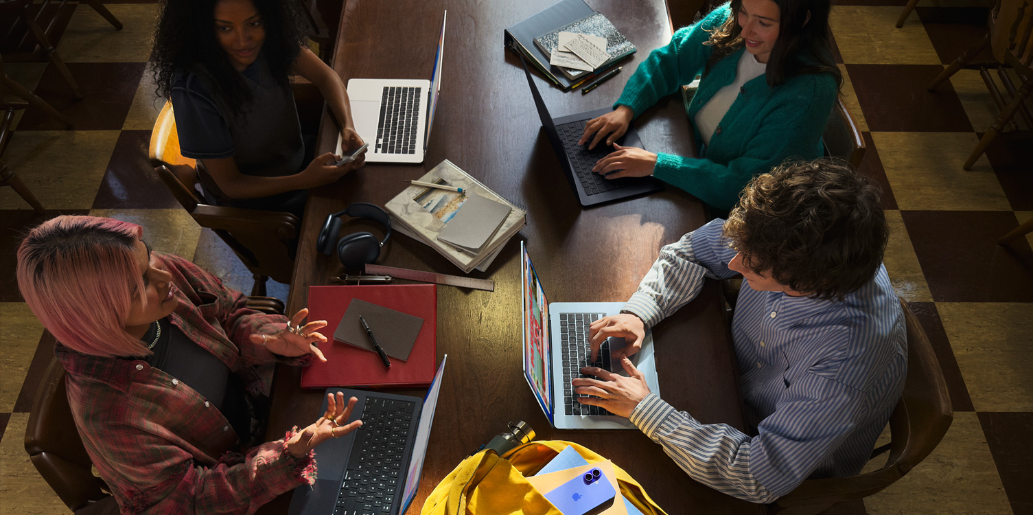 Quatre élèves autour d’une table. Les élèves sont devant leurs MacBook ouverts et leurs notes.