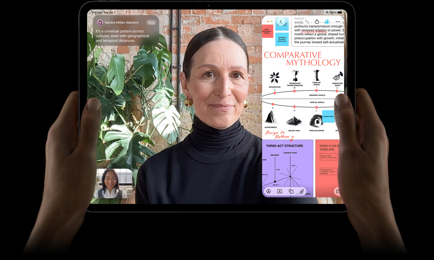 iPad Pro, front exterior, space black color, left and right hands holding in landscape orientation, rounded corners, black display bezel, display showing a FaceTime conversation being live translated, and an educational app showing a presentation of 'Comparative Mythology' with text, diagrams, and handwritten notes