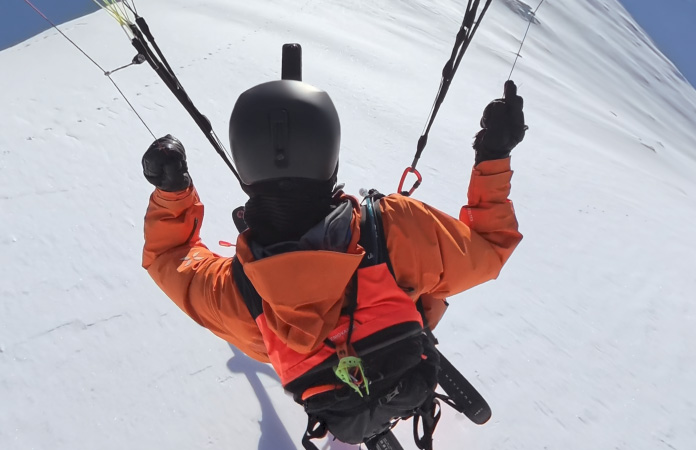 Someone paraskiing through the air across a sweeping mountaintop in wide field of view